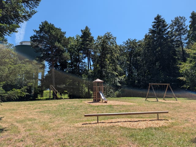 Waldspielplatz am Wasserturm Schellbronn — Spielgeräte im Waldschatten mit Blick auf den grünen Wasserturm